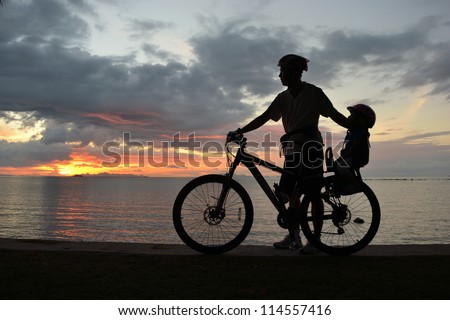 Family silhouette , daughter on child seat with parent at the beach at sunset.