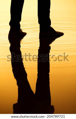 Man stand in the water with silhouette legs reflection.