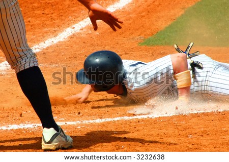 Baseball player slides by home plate with his team mate signaling safe