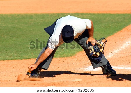 Baseball umpire dusting off dirt from home plate with a brush with his mask in his other hand