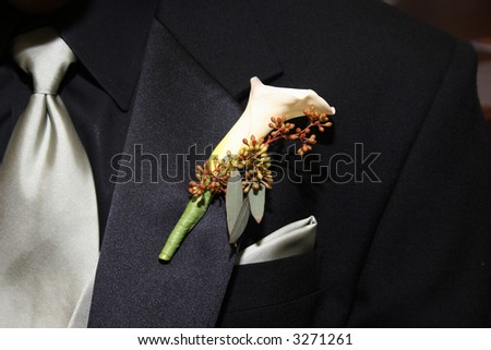 Wedding boutonniere pinned on the collar of a black wedding suit with silver tie and handkerchief