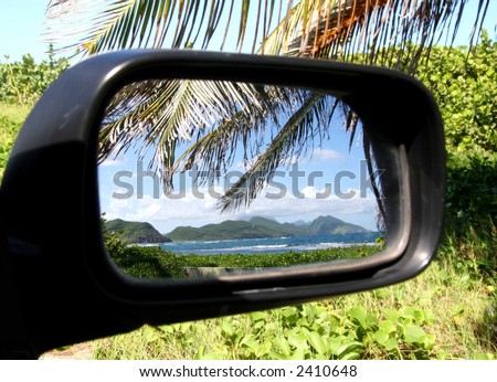 View of sea and mountains in rear view mirror of car, looking behind