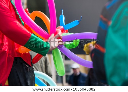 A freelance clown creating balloon animals and different shapes at outdoor festival in city centre. School bag, angel wings, butterflies and dogs made of balloons. Concept of entertainment, birthdays
