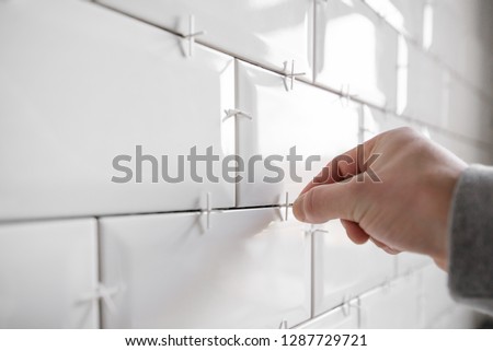 Ceramic tile lying. Installing new subway or metro tile in bathroom, shower or kitchen back splash during home renovation. Placing or taking out tile spacers with hands and pliers.