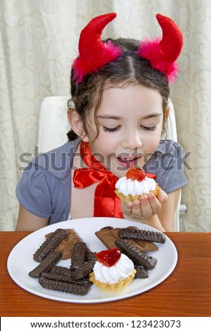 Little girl with red devil horns eats cake