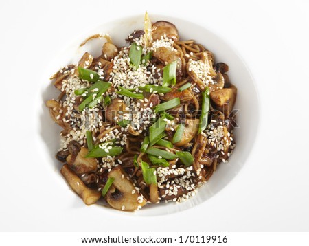 Bowl of stir fried udon noodles with mushrooms garnished with sesame seeds