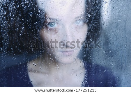 young melancholy and sad woman portrait  behind the window in the rain with rain drops on it