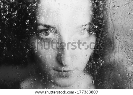 young melancholy and sad woman portrait  behind the window in the rain with rain drops on it