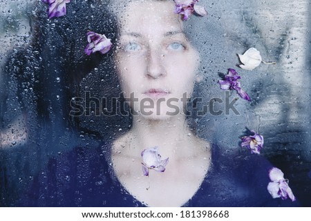 young melancholy and sad woman portrait behind the window in the rain with rain drops on it