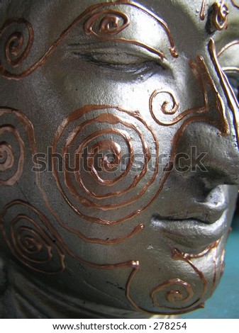 close up shot of a buddha statue with maori patterns painted on his face