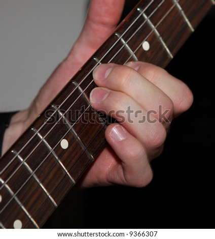 a left hand playing an electric guitar, close up
