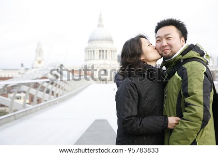 Smiling young East Asian couple at Millennium Bridge, St Paul's Cathedral in the distance.