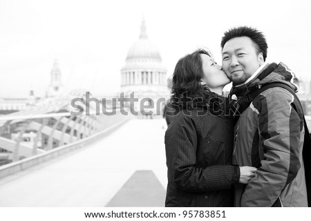Smiling young East Asian couple at Millennium Bridge, St Paul\'s Cathedral in the distance.