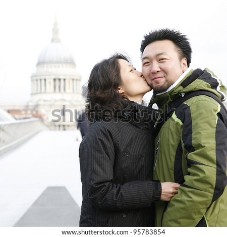Smiling young East Asian couple at Millennium Bridge, St Paul's Cathedral in the distance.