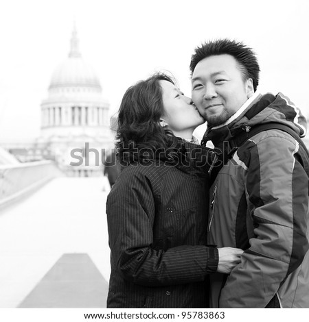 Smiling young East Asian couple at Millennium Bridge, St Paul\'s Cathedral in the distance.