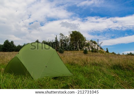 pitched tent in meadow with big rock in background - stock photo