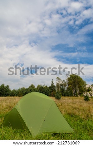 pitched tent in meadow with big rock in background - stock photo