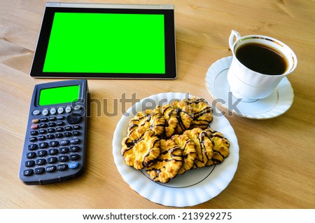 workplace with tablet pc - green box, calculator, cup of coffee and cookies - stock photo