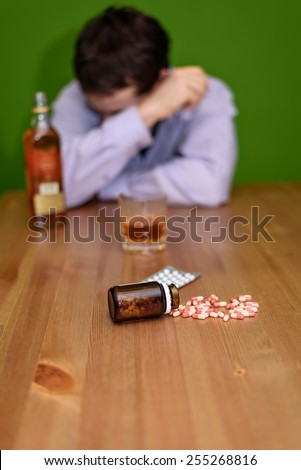depressed man drinking alcohol and taking pills on green background - stock photo