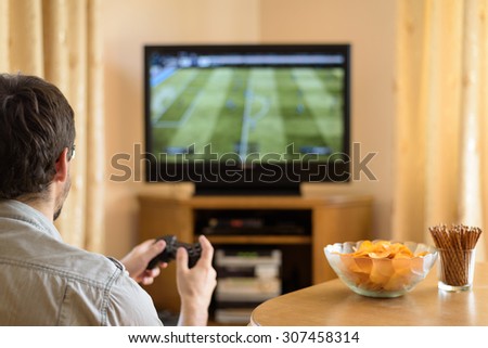 man playing soccer video game on console (television) in home - stock photo