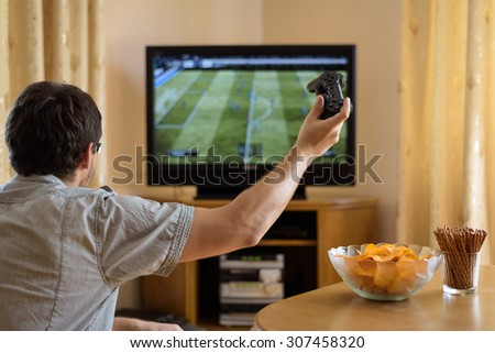 man playing soccer video game on console (television) in home - stock photo