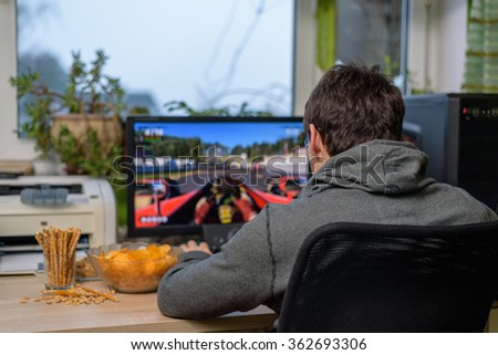 male gamer playing racing game on computer with snacks lying on table - stock photo