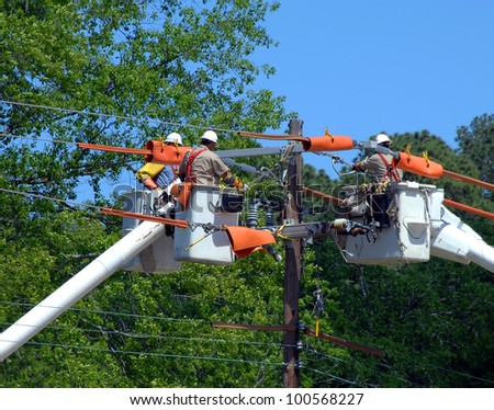 Three buckets trucks lift linemen to top of electricity pole. Three repairmen combine knowledge and repair power outage.