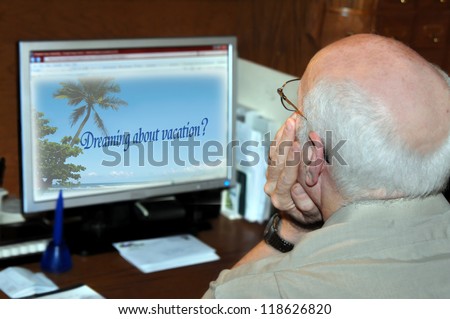 Mature male surfs the web for his dream vacation trip.  He is sitting at his desk at home with visions of palm trees and ocean breezes in his head.