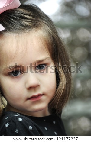 Little girl  is very solemn as she looks into the camera.  She has on a pink bow and black polka dotted shirt.