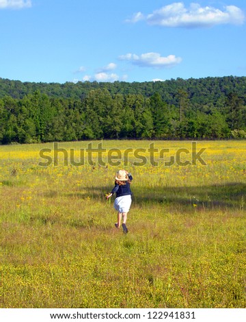 Young girl runs across a field of yellow flowers in rural Alabama.  She is holding her cowboy hat and enjoying nature.