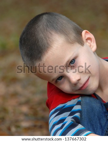 Hugging his knees are little boy, in red shirt and jeans, looks a very serious and thoughtful.