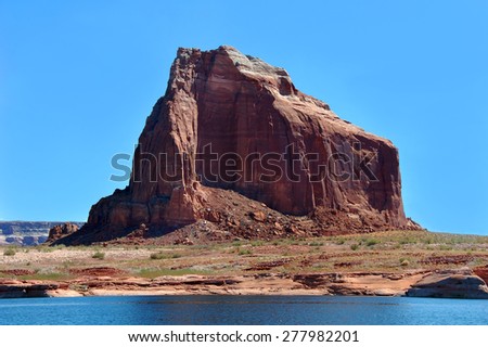 Red sandstone formation rises from the arid shoreline of Lake Powell.