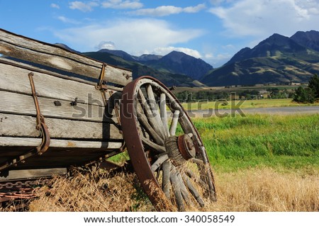 Broken down wagon is one of the few relics of the west.  Wagon faces the mountains surrounding Paradise Valley in Montana.  Weeds and grass grow around wagon.