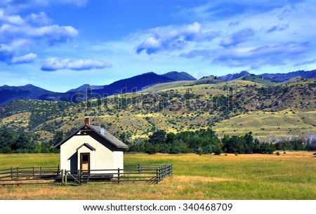 Tiny one room school house sits on the valley floor in Paradise Valley.  Wooden fence surrounds school and Gallatin Mountains rise in the back.