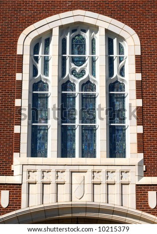 Church window has stained glass panes.  Crosses and shields embellish architecture.  Brick building.