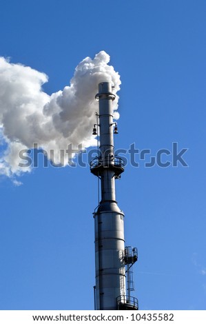 Exhaust stack releases excess steam into a vivid blue sky.  Industrial scene.