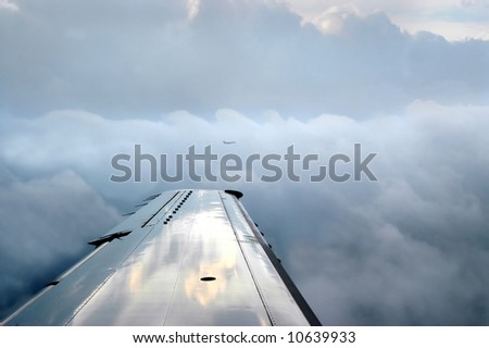 Two airplanes fly side-by-side both surrounded by clouds. Reflection of sunset is on wings.