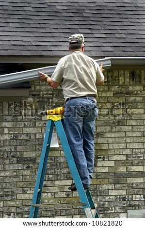 Gutters are being replaced by elderly man on a blue ladder.  Brick home.