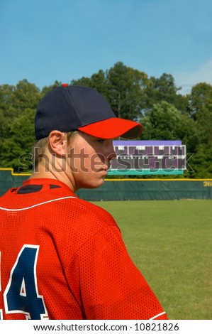 Young male teen baseball player looks sideways.  Scoreboard is in background.