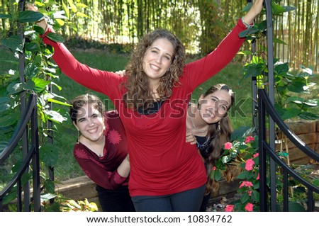 Three sisters play and have fun in a garden.  They are posing under a black metal arch with gates.