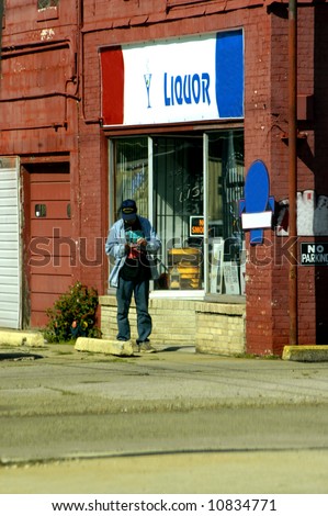 Man stands in front of liquor store and counts his change.  Weathered building and down-on-his luck man.