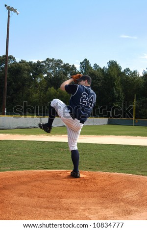 Young male teen winds up for the pitch.  Navy and white uniform.  Blue skies and baseball field.