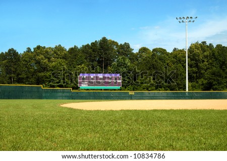 Baseball field and scoreboard includes grass, fence, lights and blue sky.