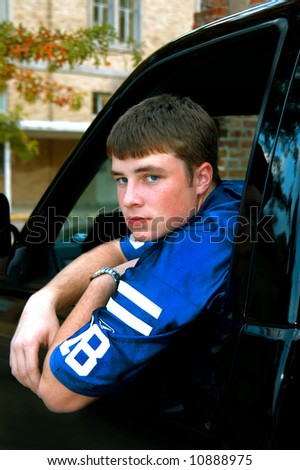 Young male teen leans out of his truck window.  Serious expression on his face.  Blue jersey.