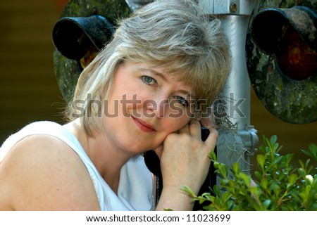 Middle aged woman leans against a railroad signal.  Crossing from young to old.