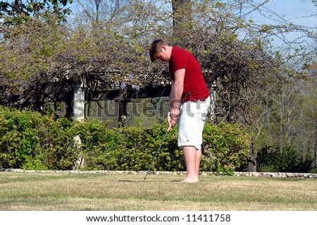 Garden setting in background of golf shot.  Male teen has on shirts and red polo.