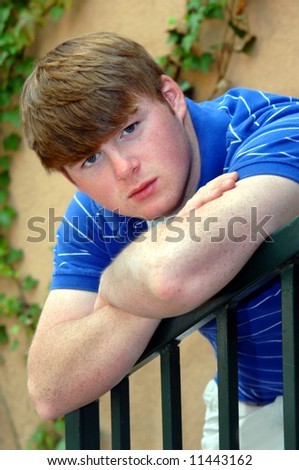 Arms crossed, this male teen leans against a green metal rail.