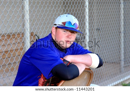 Baseball player leans over the back of metal chair during lull in game.