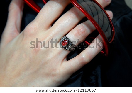 Class ring is proudly worn by female teen.  She is also holding red rimmed sunglasses.
