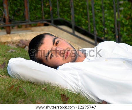 Enjoying an afternoon outdoors, male teen lays back against grassy hill.  White shirt.